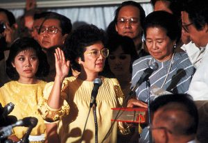 Corazon Aquino stands before a crowd in a yellow top.